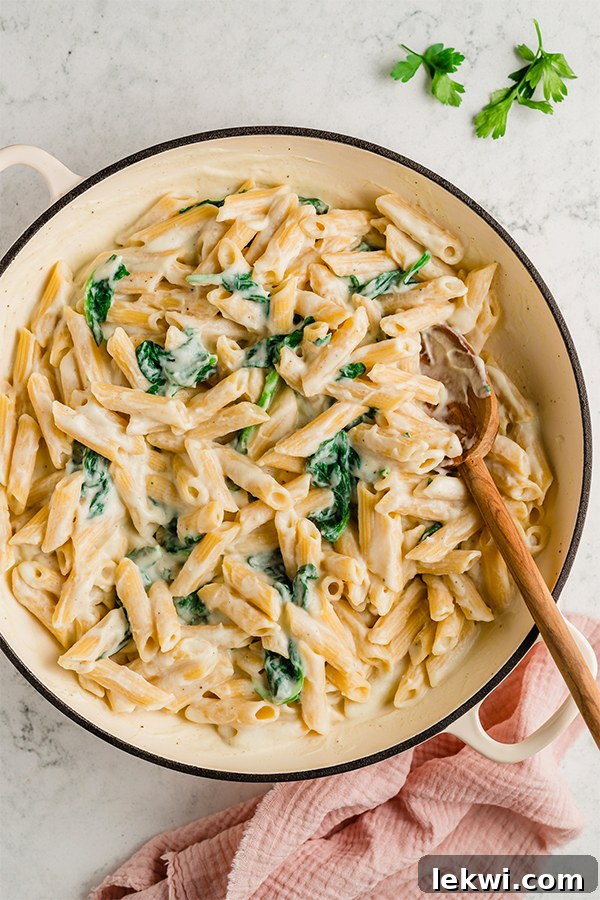 A pot of Easy Penne Alfredo with a wooden spoon in it, showing the completed dish with pasta and sauce.