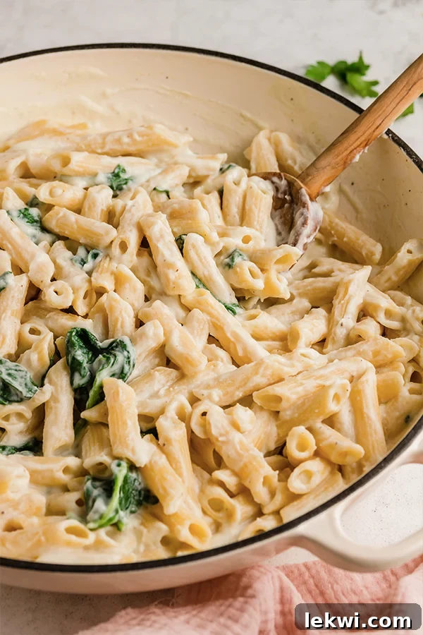 Penne alfredo in a pot with a wooden spoon.