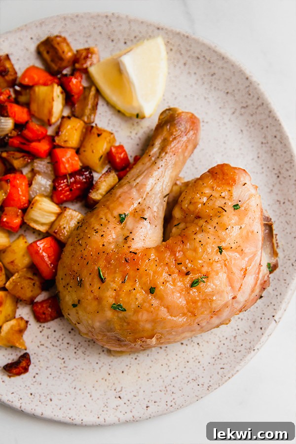 A serving of roasted spatchcocked chicken with mixed root vegetables and a lemon wedge, on a white plate.