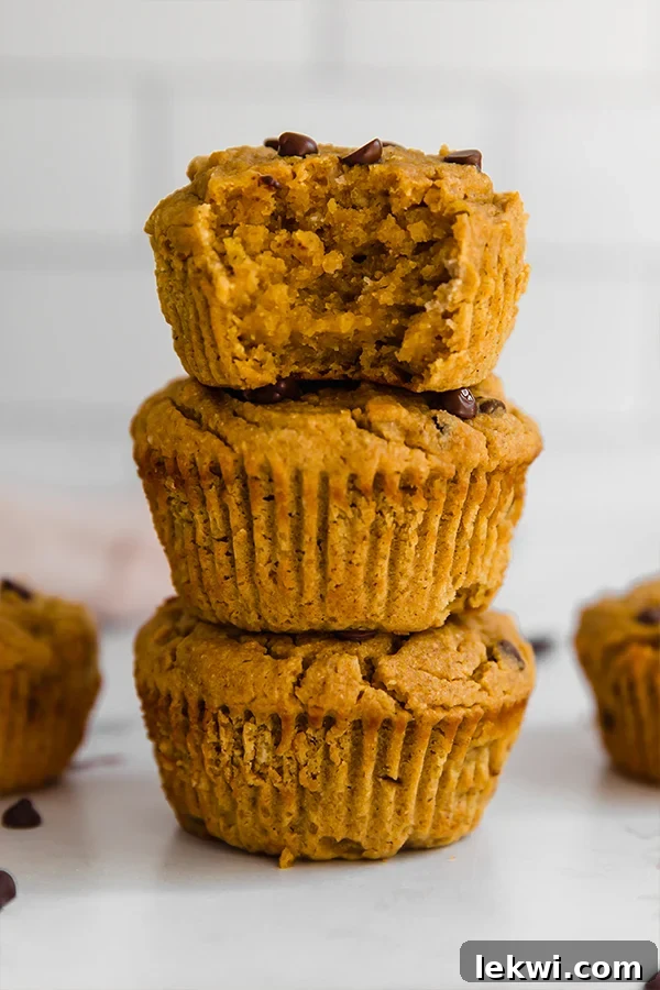 A stack of golden-brown paleo pumpkin muffins, with one showing a bite taken out, inviting you to taste.