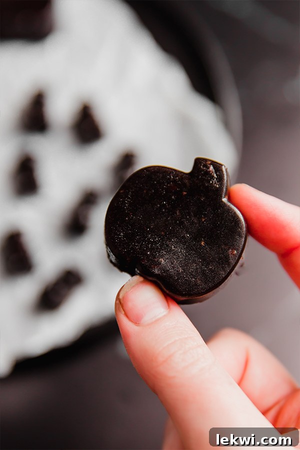 A spooky gummy molded into a pumpkin being held by a few fingers.