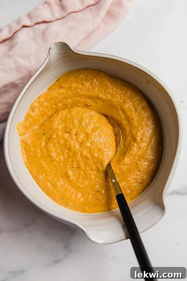 A high-speed blender container filled with vibrant orange butternut squash pasta sauce.