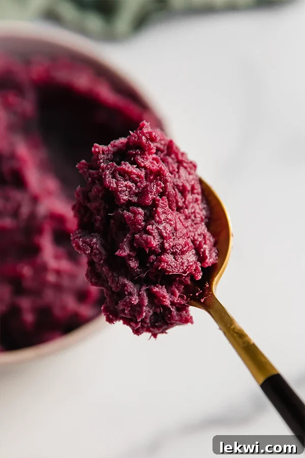 A close-up shot of a spoonful of purple mashed sweet potatoes, showing their creamy texture and rich color.