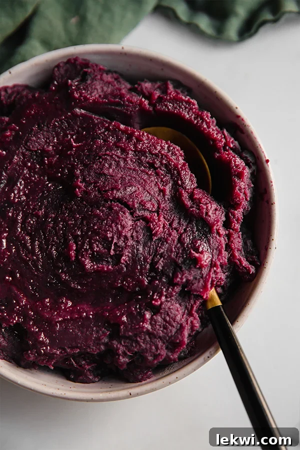 Spoon scooping purple mashed sweet potatoes from a serving bowl, showcasing the creamy texture.