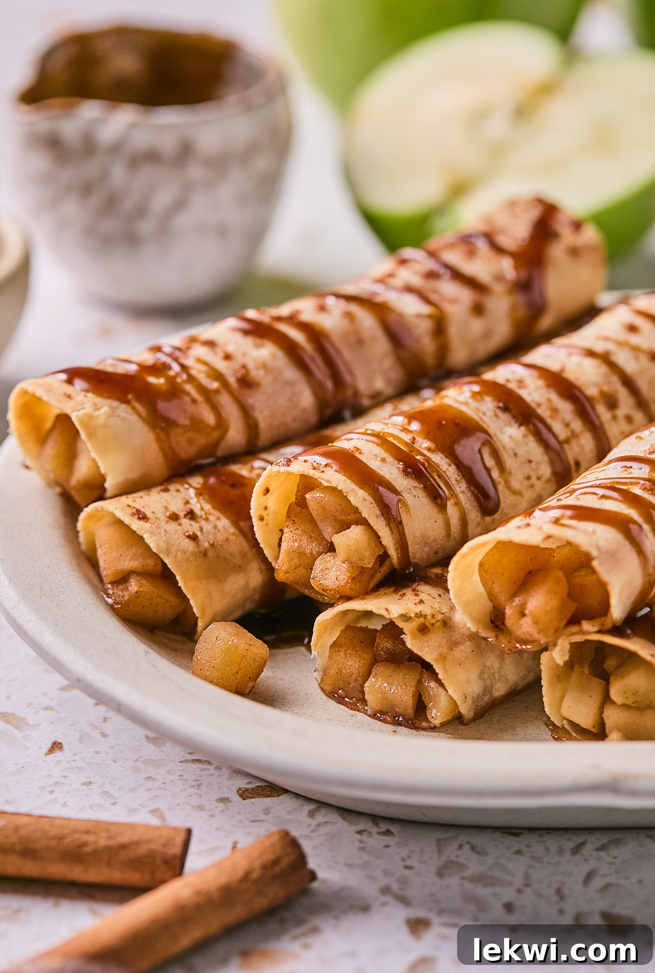 Close-up of Apple Pie Roll-Ups on a plate, generously drizzled with caramel and additional caramel on the side for dipping.