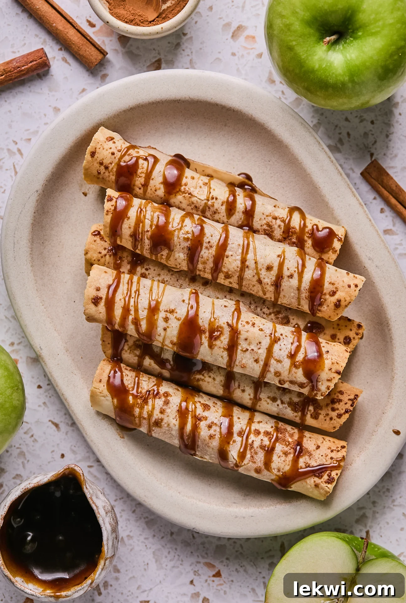 Apple pie roll ups on a platter drizzled with caramel.