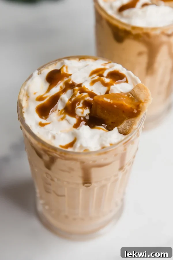 A tall glass filled with a creamy, spiced pumpkin pie milkshake, garnished with a drizzle of caramel, a dollop of coconut cream, and a small wedge of pumpkin pie.