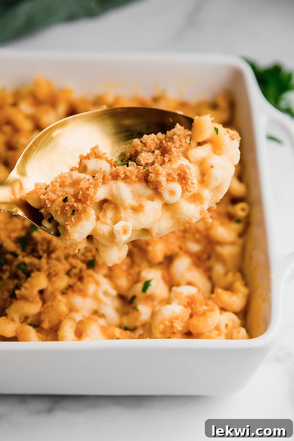 A spoon digging into a dish of creamy paleo mac and cheese with a crispy topping.