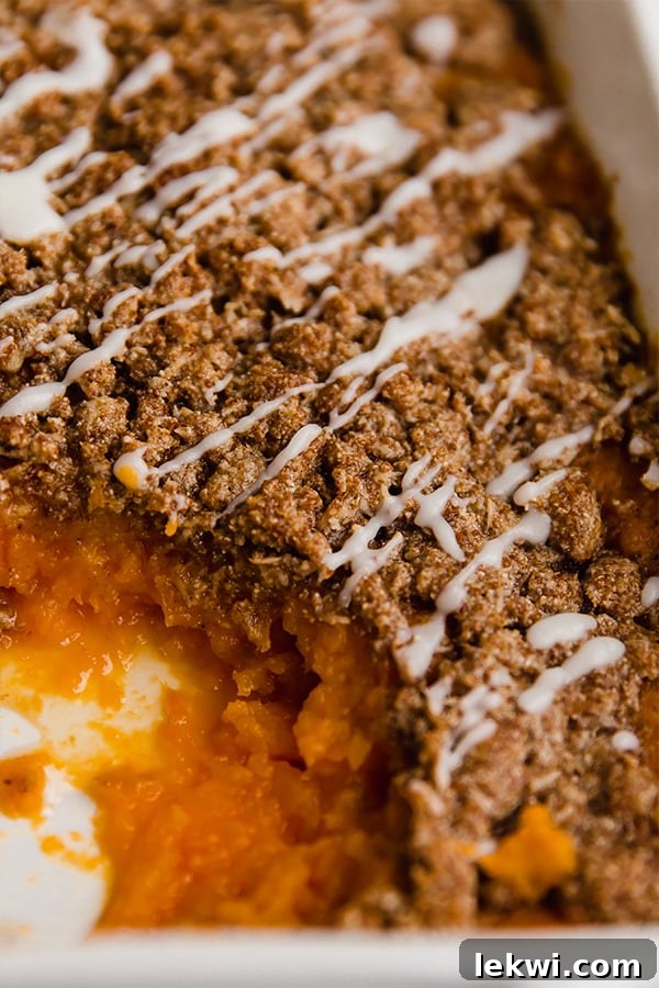 A baking dish of sweet potato casserole, with a section scooped out to reveal the creamy interior and crunchy topping.