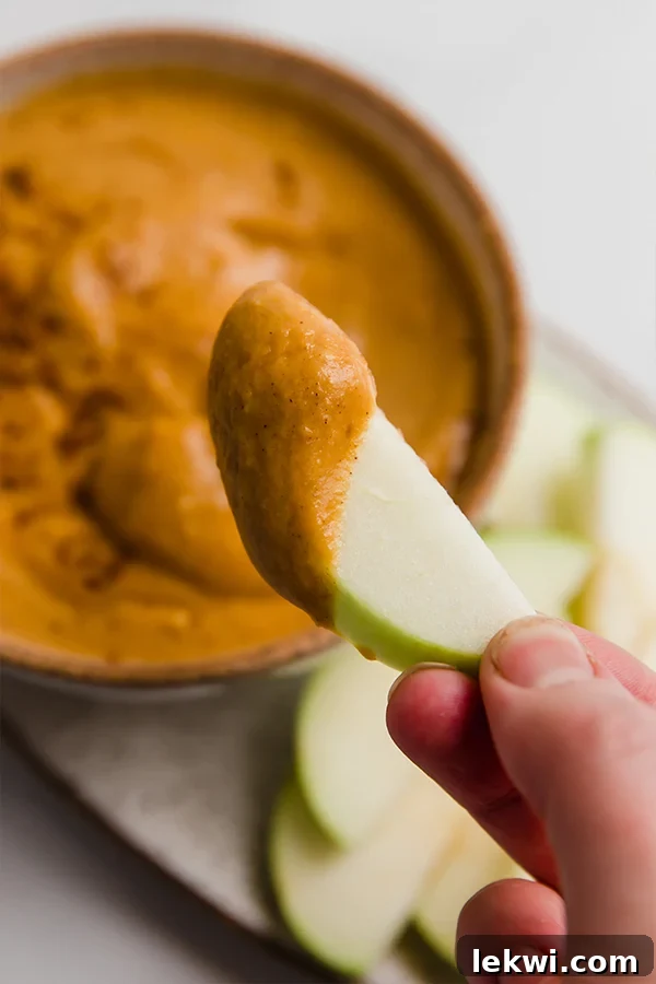 A crisp apple slice, generously covered in a thick layer of creamy pumpkin pie dip, ready to be enjoyed. The rich texture and vibrant color of the dip are showcased, emphasizing its appealing consistency and deliciousness.