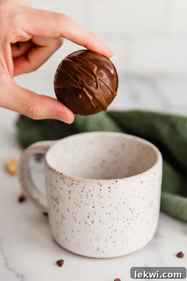 Person holding a hot cocoa bomb over a speckled mug.