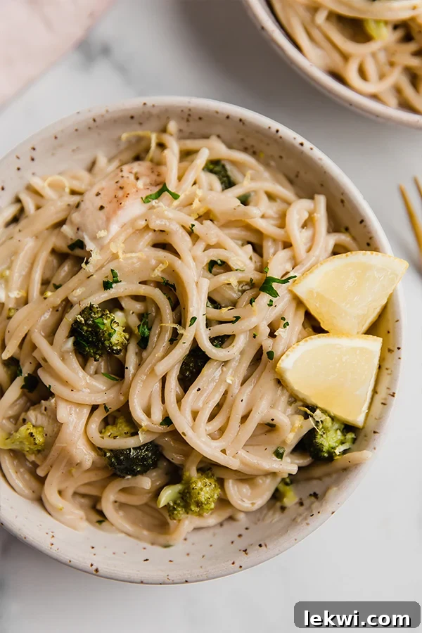 Lemon chicken pasta in a bowl with lemon wedges, garnished with fresh parsley.