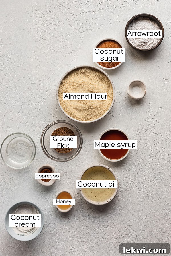 A selection of fresh ingredients including almond flour, espresso powder, coconut sugar, coconut oil, and a can of coconut cream, laid out on a surface.