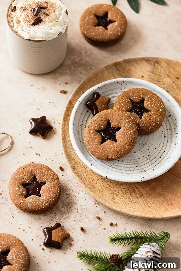 Gingerbread sandwich cookies with star cutouts on a plate, showcasing their festive appeal and delicious chocolate filling.