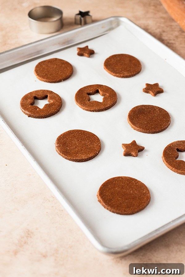 Gingerbread cookie dough rolled out and cut into circles, with smaller star shapes removed from some, ready for baking.