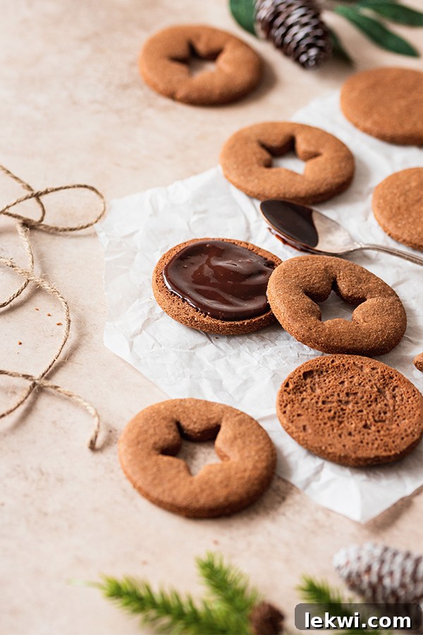 Assembling chocolate gingerbread sandwich cookies, with ganache being spread onto a cookie base and a cutout cookie placed on top.