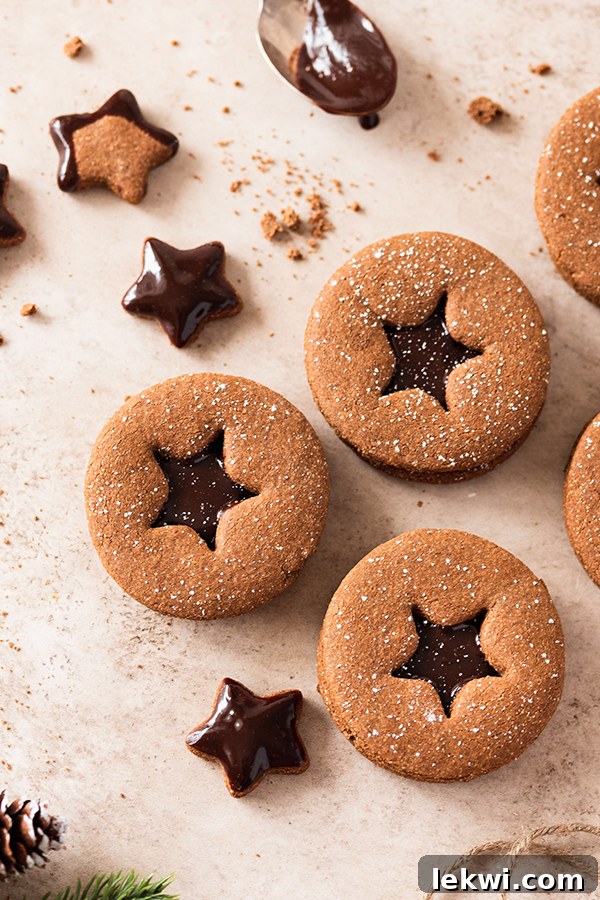 Several finished chocolate gingerbread sandwich cookies stacked and displayed, showing their dusted tops and ganache filling.