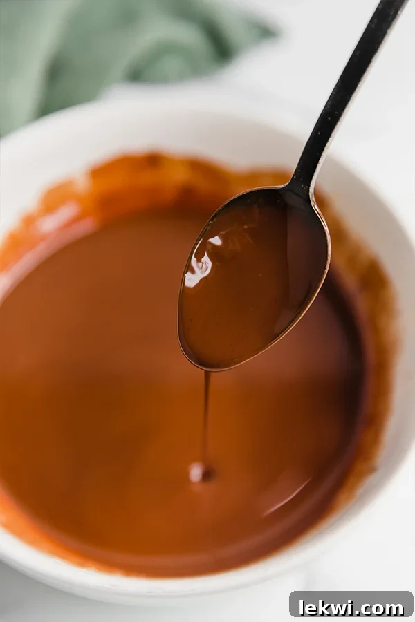 A spoon drizzling rich, melted dairy-free chocolate, illustrating the smooth consistency perfect for coating.