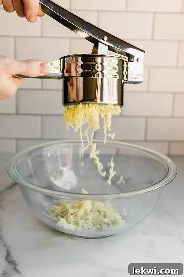 Ricing sweet potato directly over a clear glass bowl, showing the fine, fluffy texture.