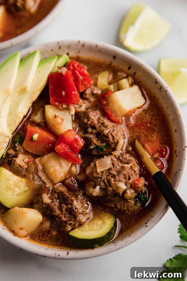 A bowl of Albondigas soup, garnished with fresh cilantro and avocado slices.