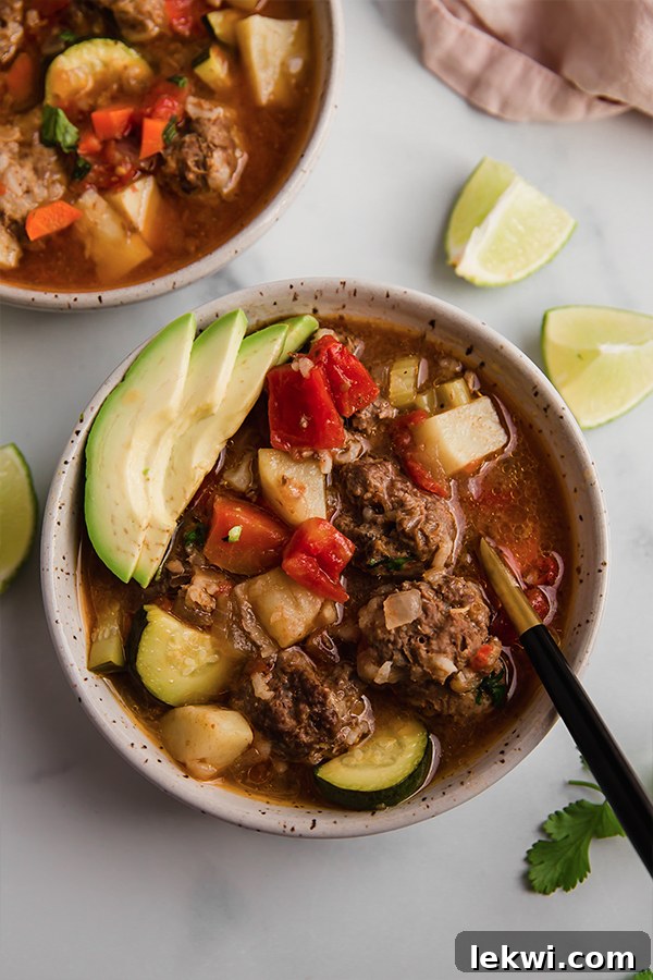 A bowl of Albondigas soup with a spoon, showing the rich broth and meatballs.