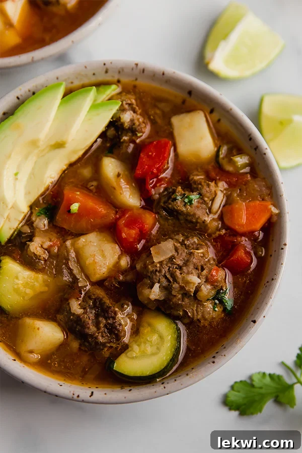 A bowl of Mexican meatball soup, garnished with fresh herbs and avocado.