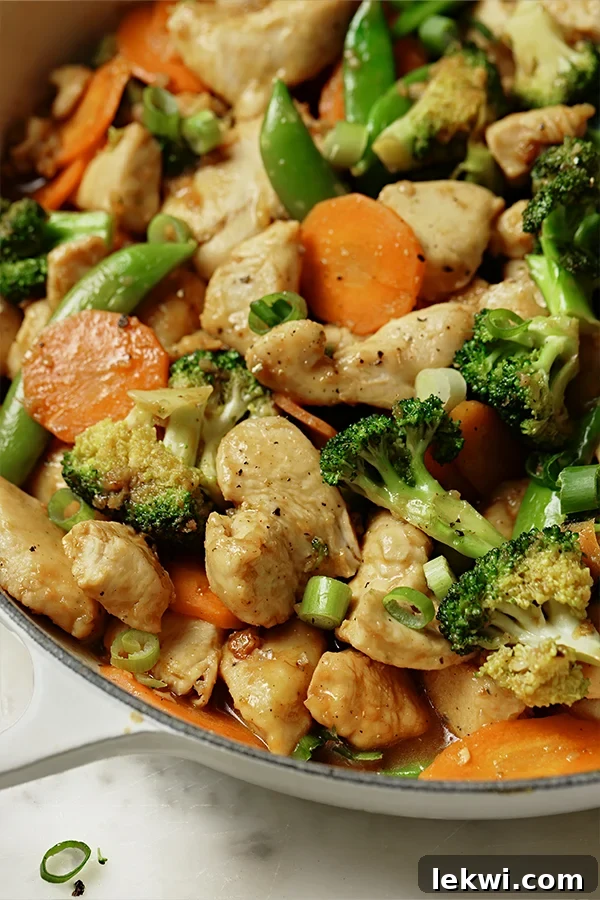 Vibrant orange chicken stir fry with broccoli, carrots, and sugar snap peas ready to be served.