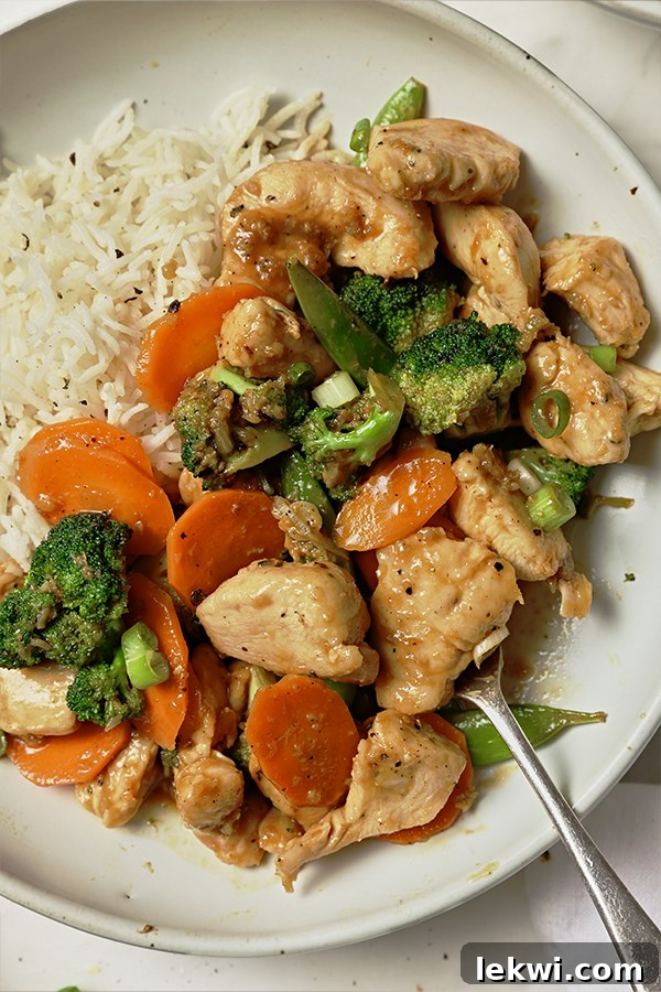 A perfectly plated serving of orange chicken stir fry alongside a bed of white rice, garnished with green onions.