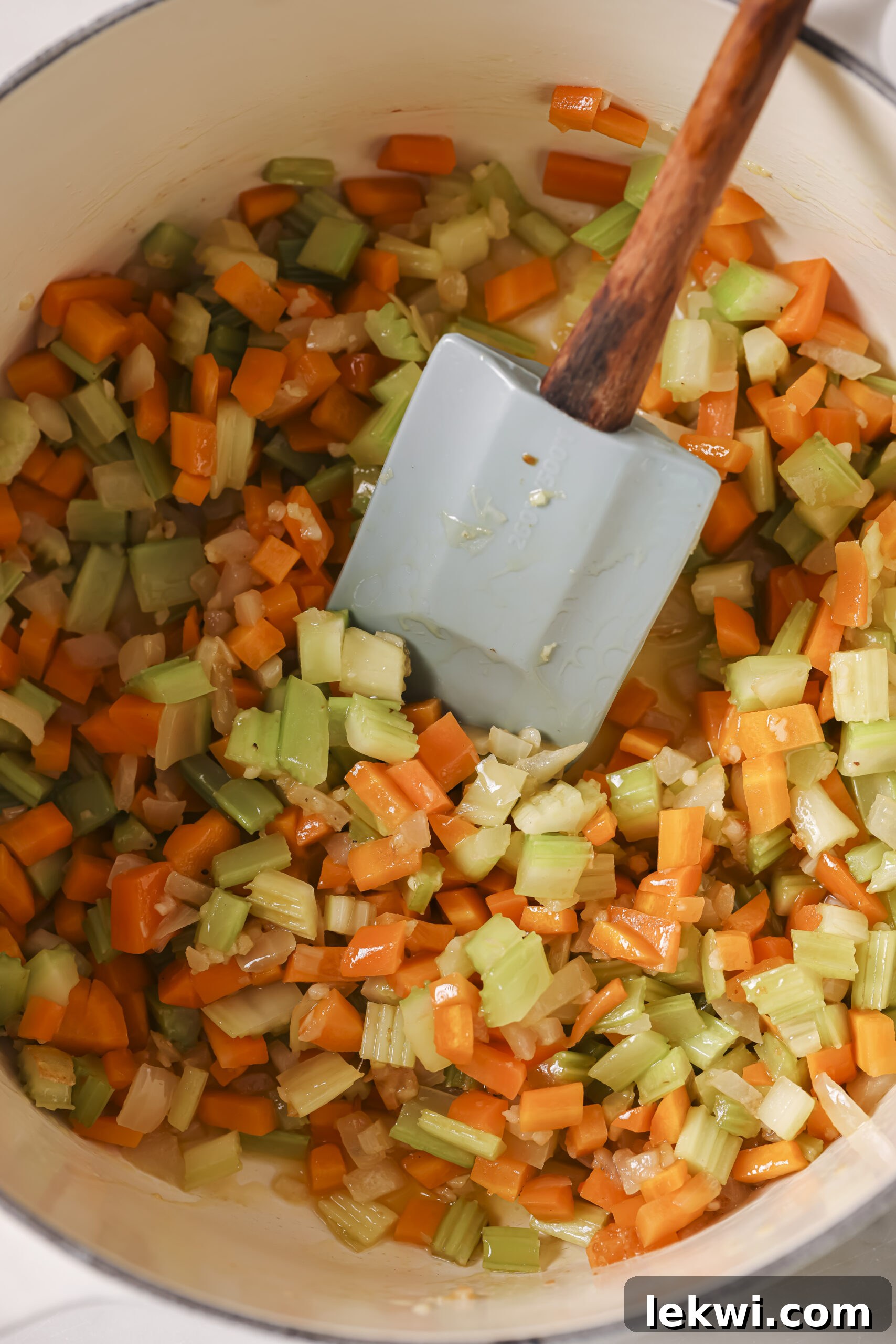 Chopped carrots, onion and celery in a large white pot, sautéing with a spatula.