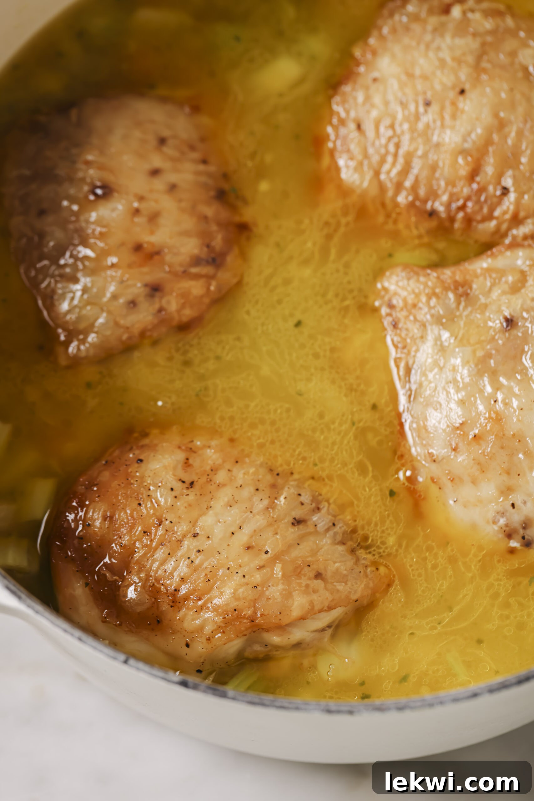 Carrots, onion and celery in a pot with broth and seared chicken thighs, ready to cook in the oven.