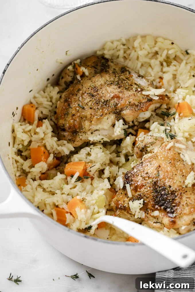 One pot baked chicken and rice in a large white pot, topped with fresh herbs, with a spoon dipping into the pot.