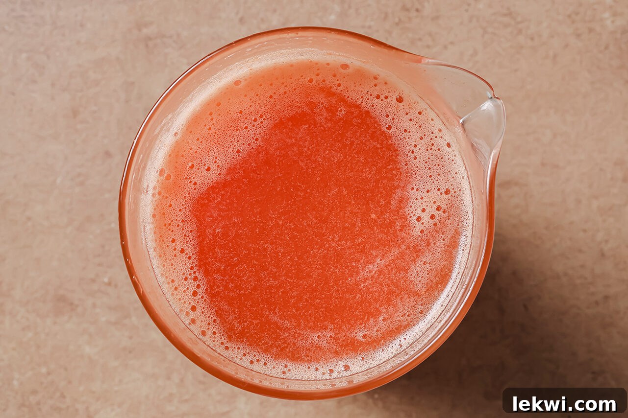 Vibrant red tomato broth prepared in a glass container, ready to be added to the soup.
