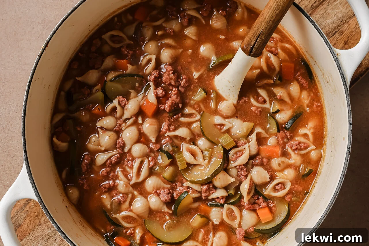 Finished Conchitas con Carne soup simmering in a white Dutch oven, with tender pasta and vegetables.