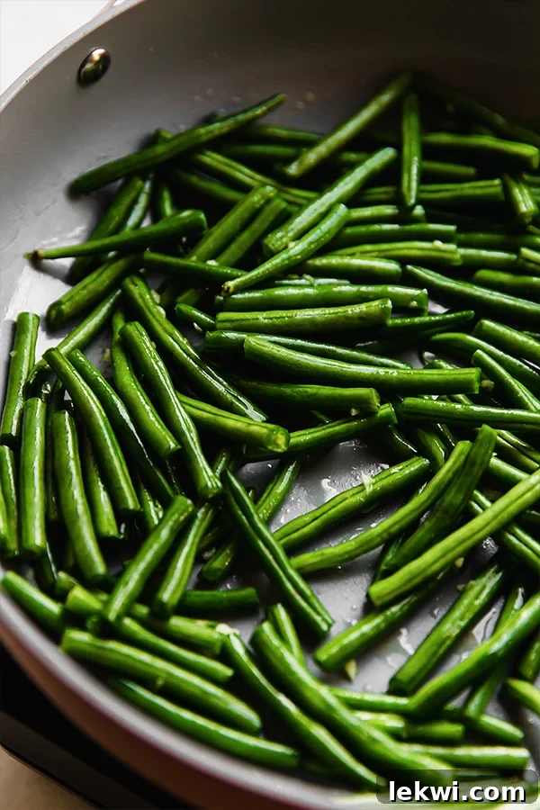Fresh green beans and minced garlic sizzling in ghee in a large skillet, beginning to soften.