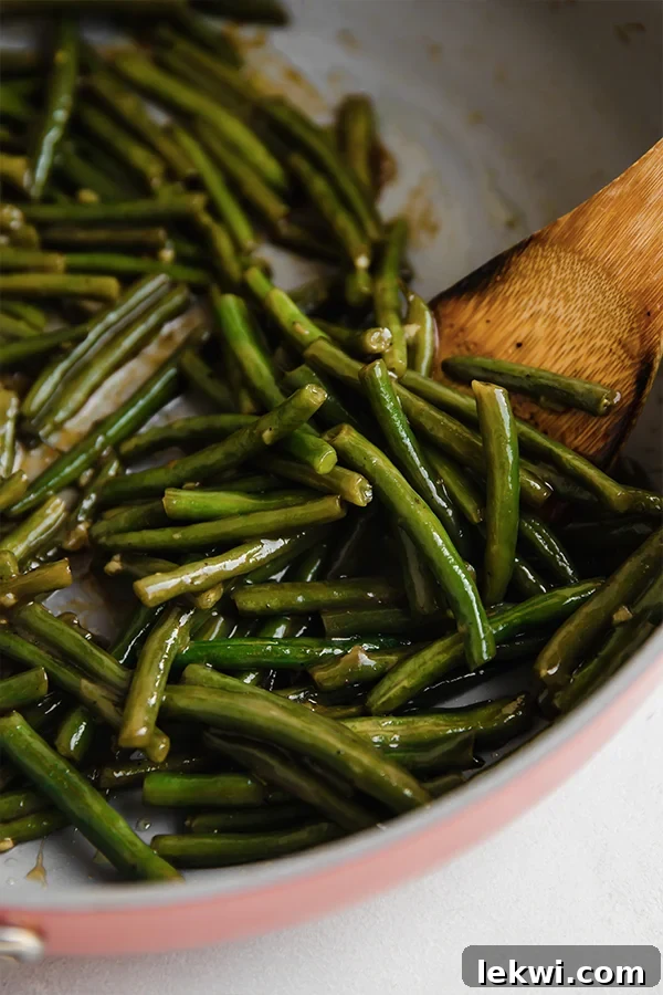 Green beans coated with arrowroot starch, with hot water, coconut sugar, and apple cider vinegar added, being stirred.