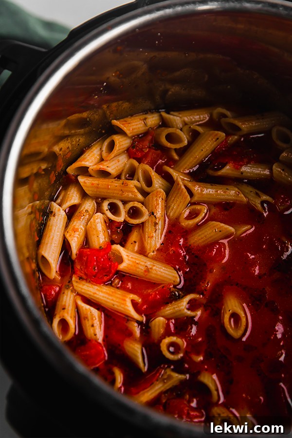 Uncooked gluten-free pasta, marinara sauce, and broth layered in the Instant Pot before cooking.