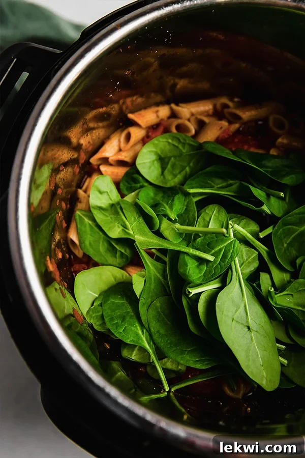 Fresh spinach being stirred into the cooked gluten-free Instant Pot pasta.