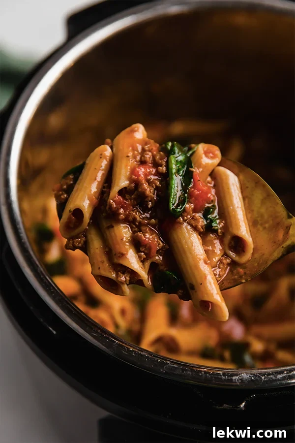A spoon scooping a generous portion of cooked gluten-free Instant Pot pasta with beef and spinach.