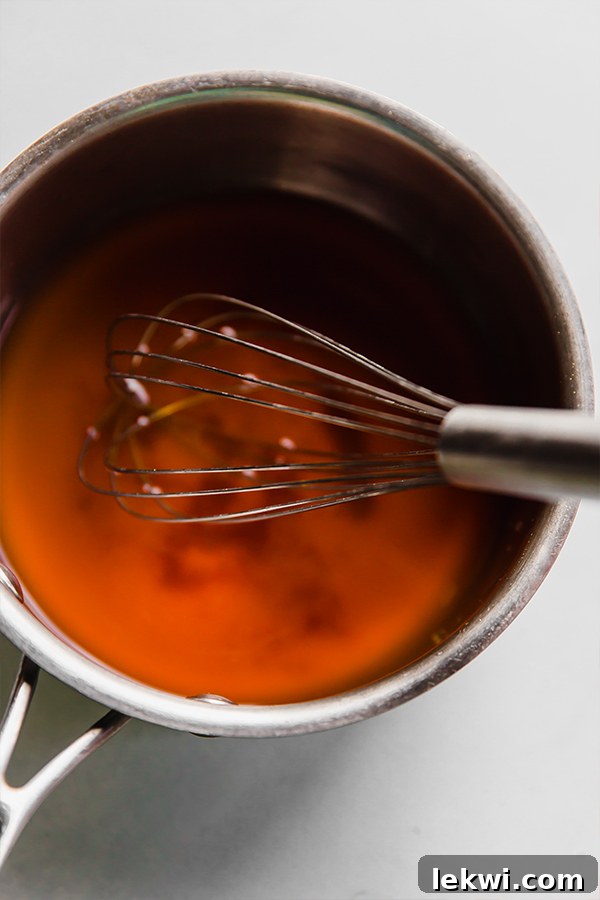 A whisk in a pot dissolving the coconut sugar in the liquid for pickled ginger.