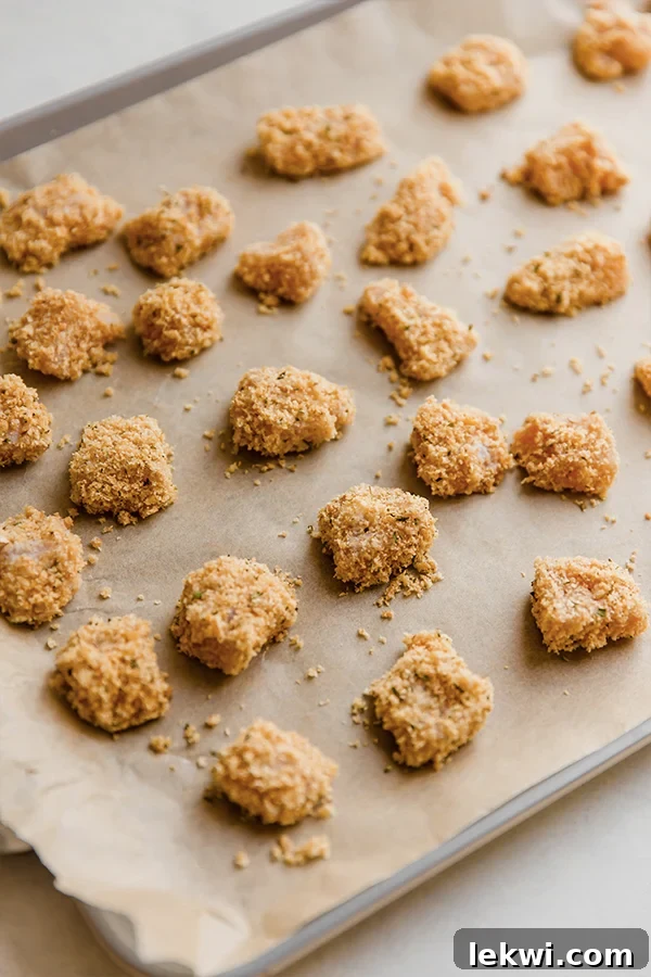 Raw pork panko chicken nuggets arranged in a single layer on a parchment-lined baking sheet, ready for the oven.