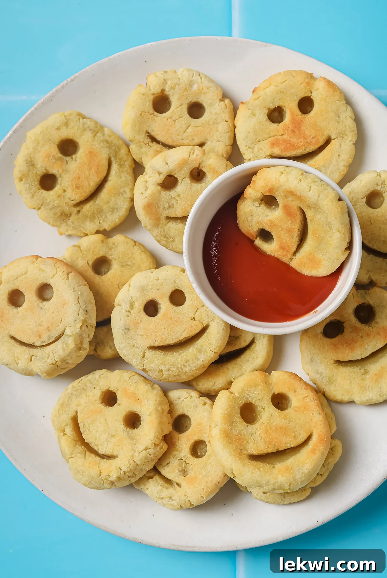 Golden sweet potato smiley fries on a white plate with a side of dipping sauce, evoking a sense of healthy and fun eating.