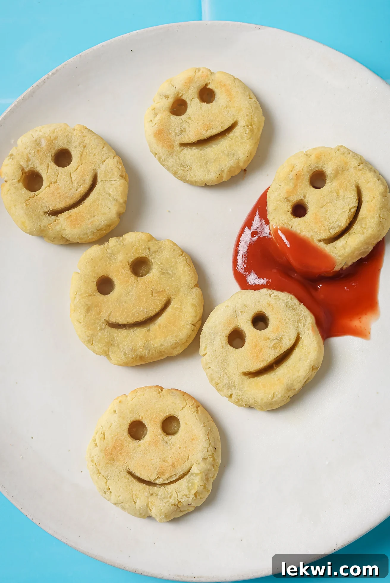 A close-up of baked sweet potato smiley fries on a white plate, served with a small bowl of ketchup for dipping, highlighting their inviting texture and fun shape.