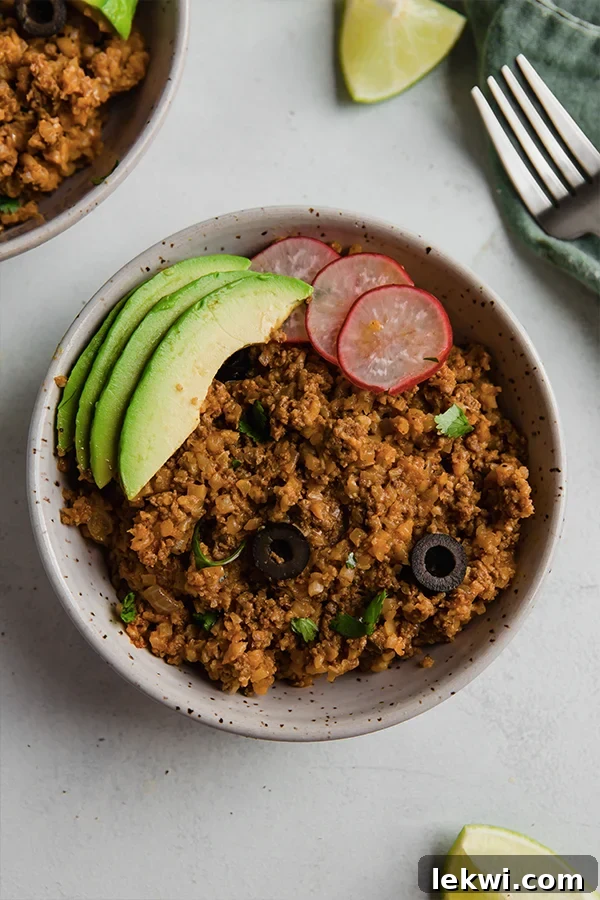 A vibrant, well-composed bowl of ground beef and cauliflower rice enchilada, topped generously with avocado slices.