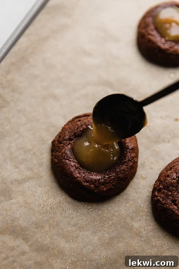 Filling the brownie cookies with caramel on a baking sheet.