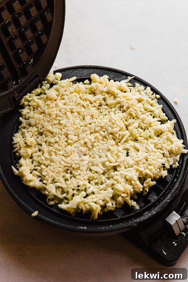 Sweet potato hashbrown mixture cooking on a hot, greased waffle iron, forming into a waffle.