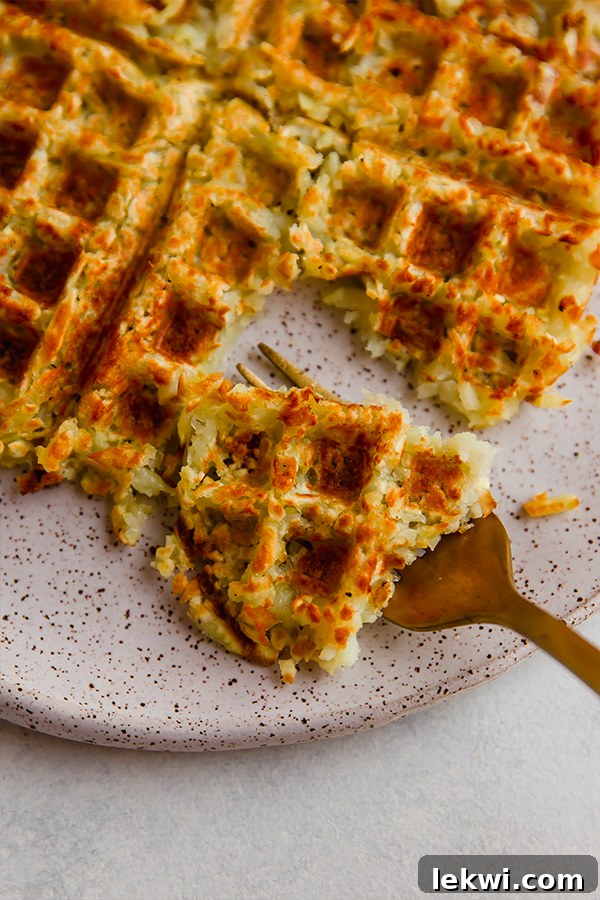 A fork taking a bite out of a sweet potato hashbrown waffle on a plate, showing the crispy texture.