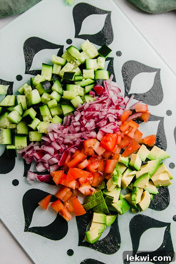 A vibrant bowl filled with diced cucumbers, tomatoes, red onion, avocado, and fresh herbs, ready for Greek salsa.