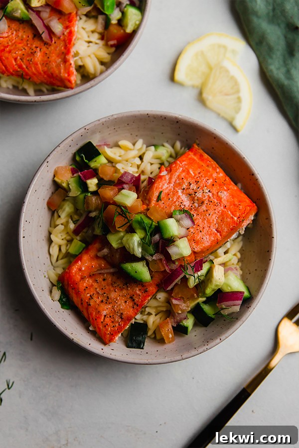 A beautifully arranged Greek Salsa Salmon Bowl, featuring a golden salmon fillet topped with vibrant salsa, all resting on a bed of grain.