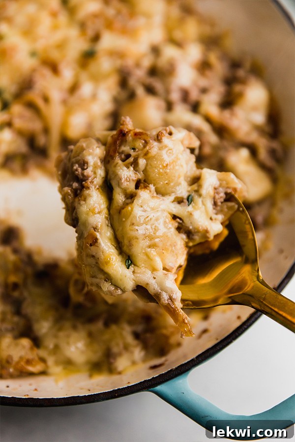 A spoonful of French Onion Gnocchi Skillet lifted from the pan, showing the creamy sauce, gnocchi, and onions.