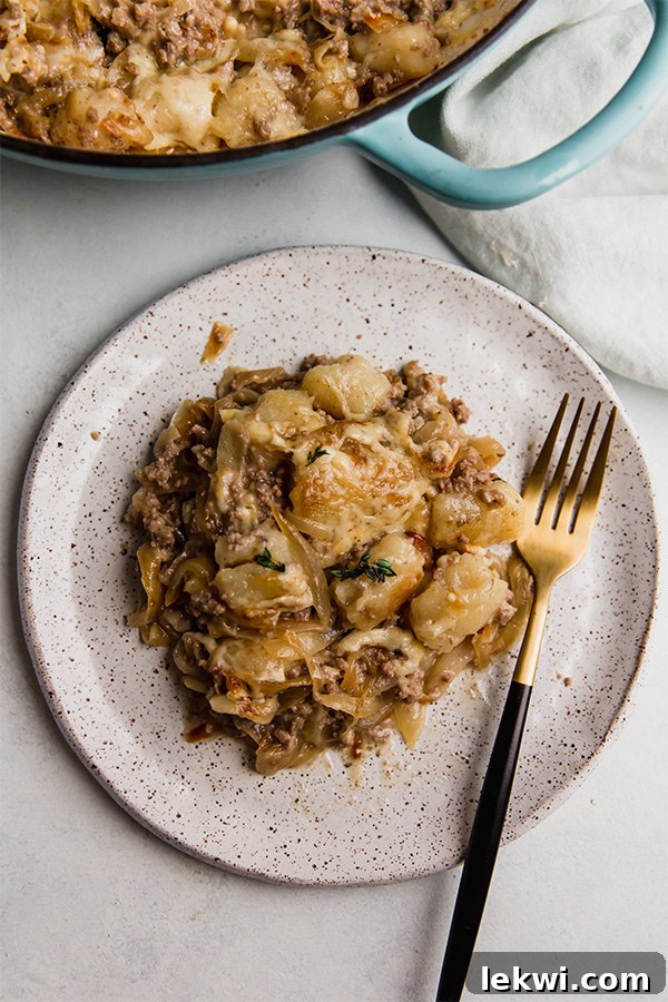 A beautifully plated serving of French Onion Gnocchi Skillet, garnished with fresh thyme, against a rustic background.